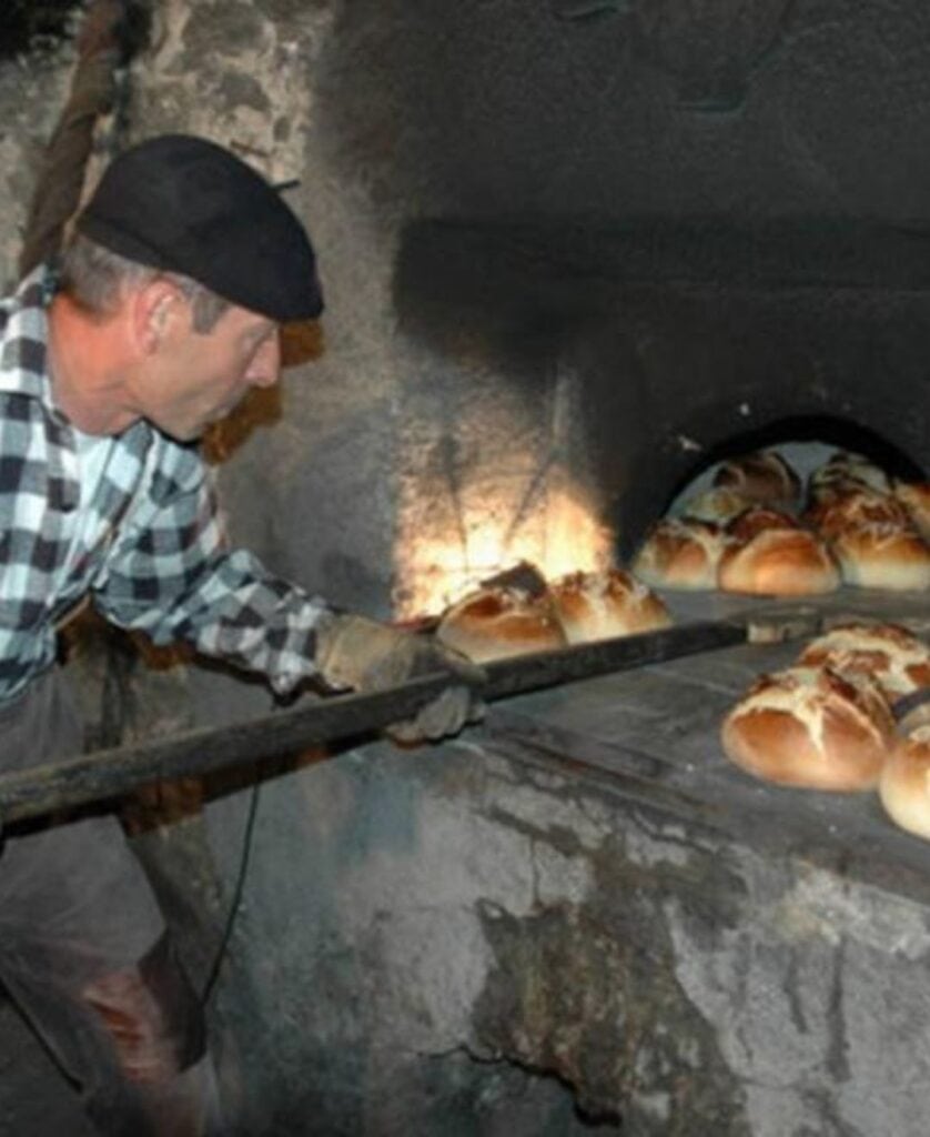 A baker in traditional attire removes golden loaves from a rustic wood-fired oven during the Fête du Pain in Longefoy, a charming July event celebrating La Plagne’s alpine bread-making heritage.