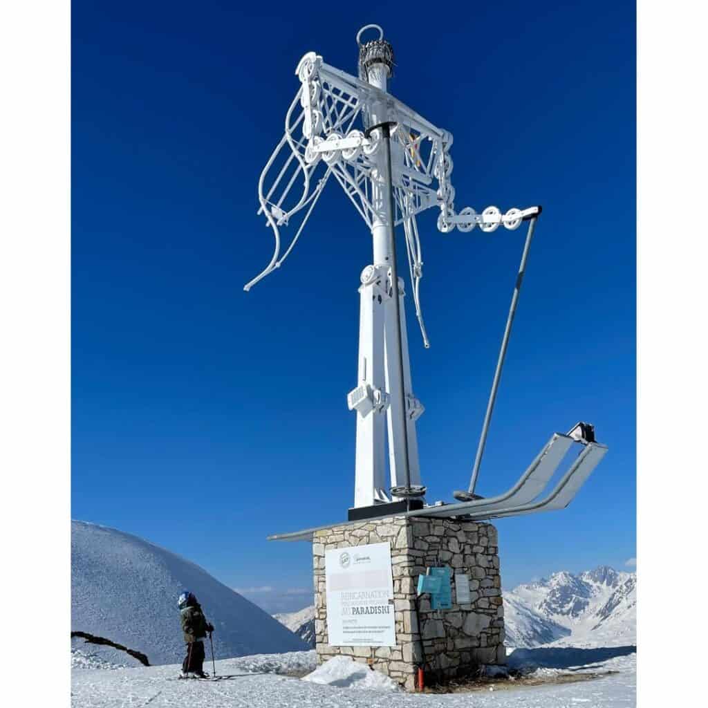 A child skier stands next to the striking white ski-angel monument at Arpette in La Plagne, a scenic and peaceful picnic spot with panoramic mountain views and a unique alpine landmark.
