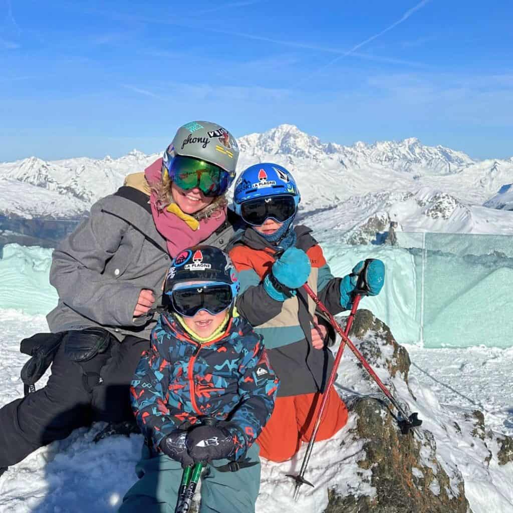 A smiling family in ski gear poses at the Live 3000 viewpoint in La Plagne, one of the best picnic spots for breathtaking views of Mont Blanc and the surrounding snowy peaks.