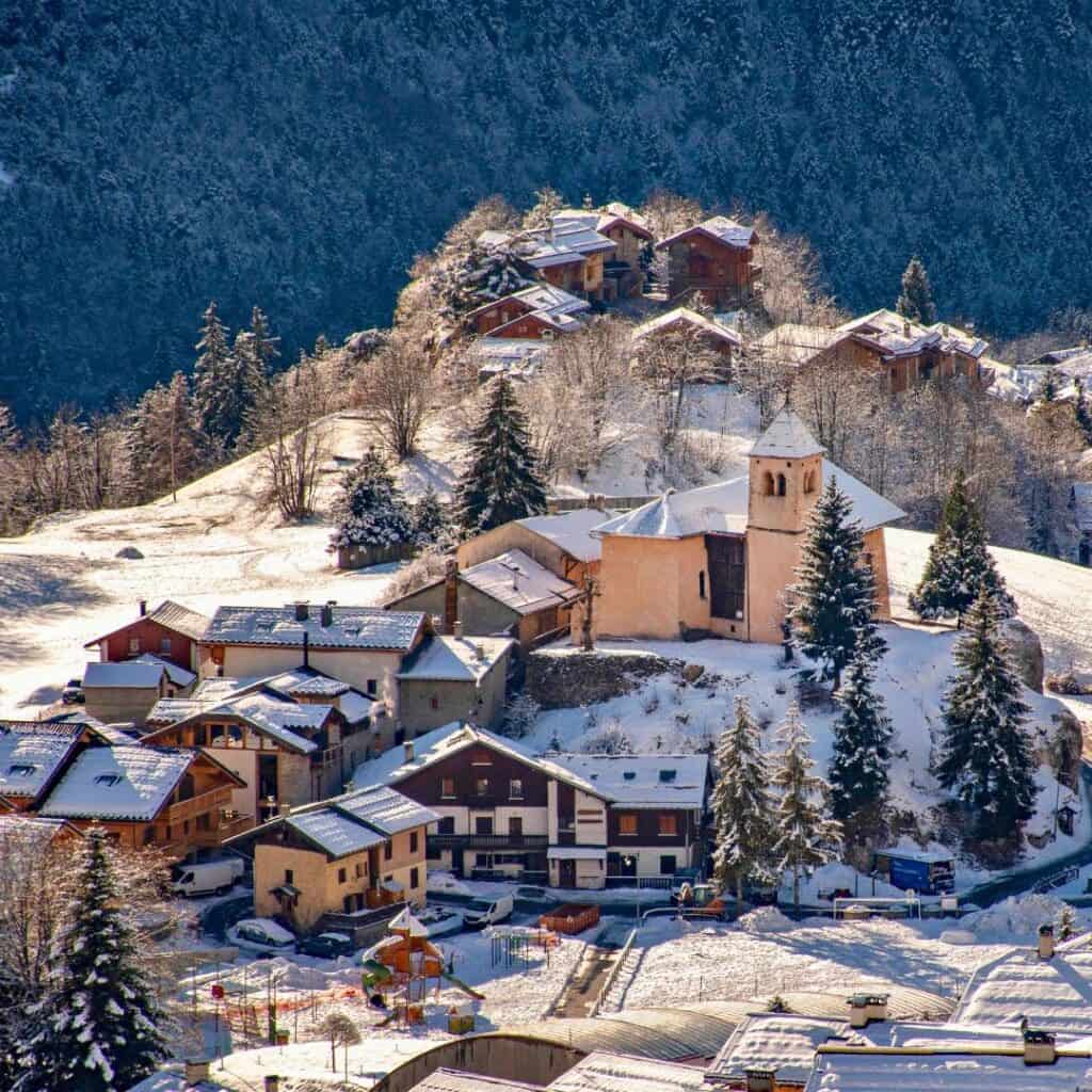 Quaint historic buildings and a small chapel in Champagny La Plagne, perched on a snowy hillside with surrounding pine trees and a peaceful alpine village feel.