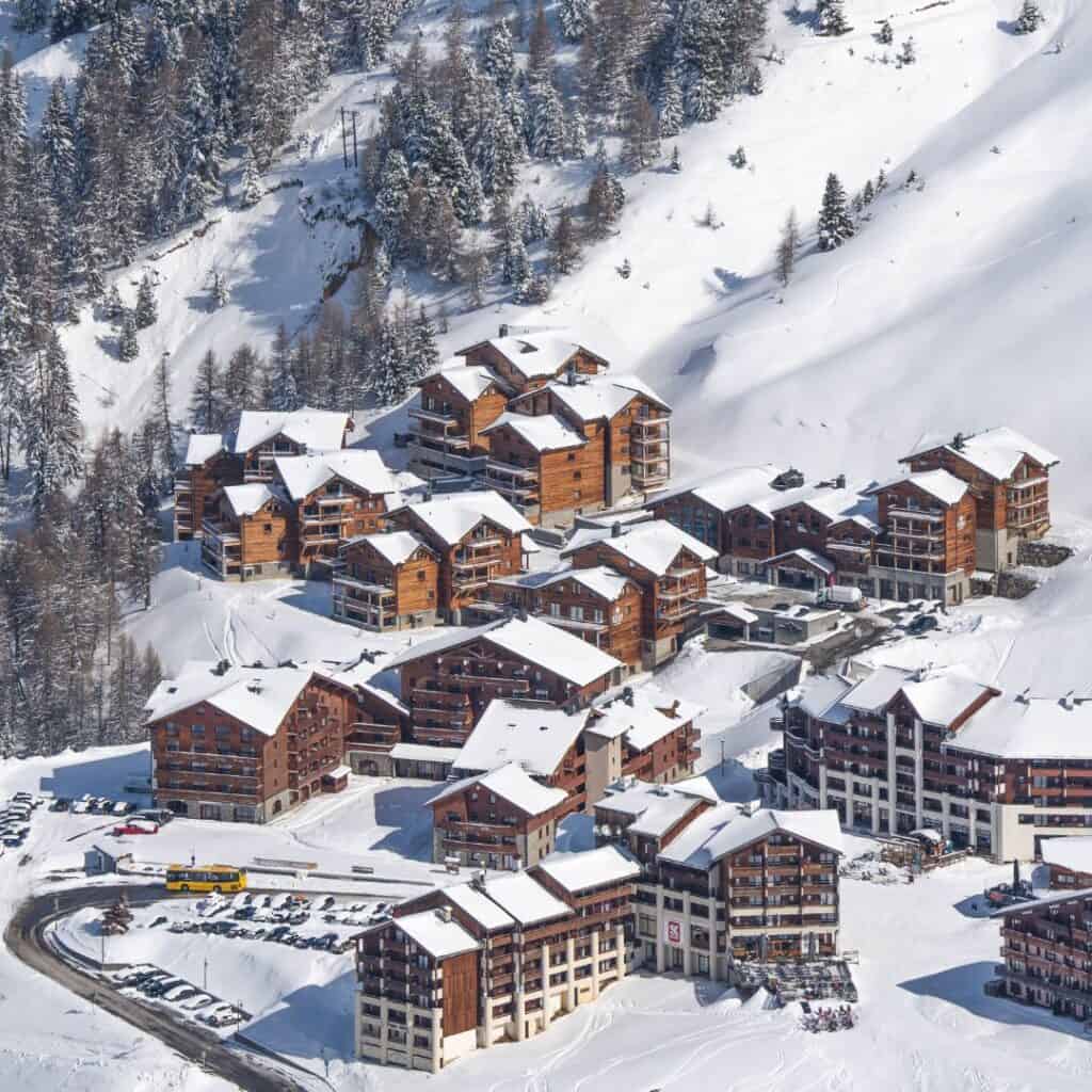 Cluster of traditional wooden chalets and mid-size lodges nestled into the snowy hillside of Plagne Soleil, one of the 11 La Plagne villages, surrounded by pine trees and ski slopes.