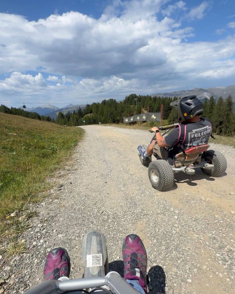 Mountain carting on a wide alpine track above Montalbert with chairlifts and green summer mountains in the background.