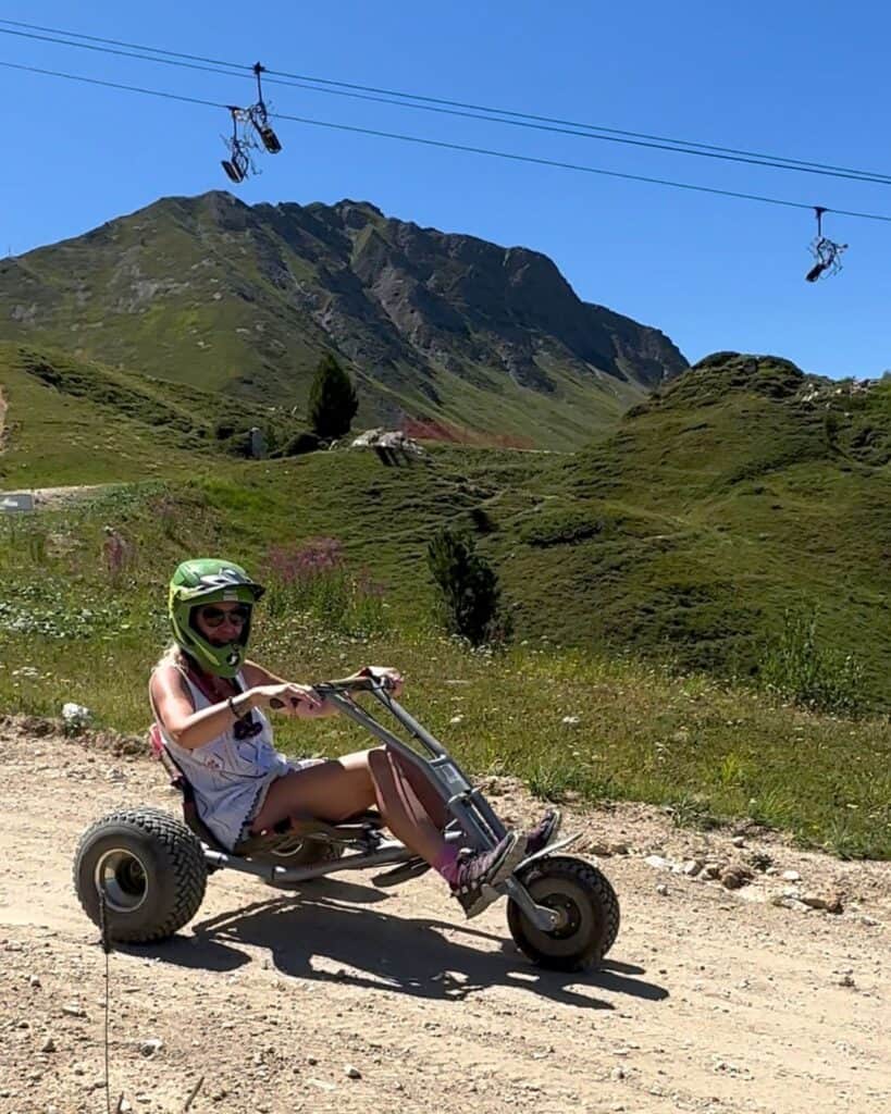 Mountain carting down a forest track in Plagne Centre, La Plagne, with gondola cabins and mountain views in the background.