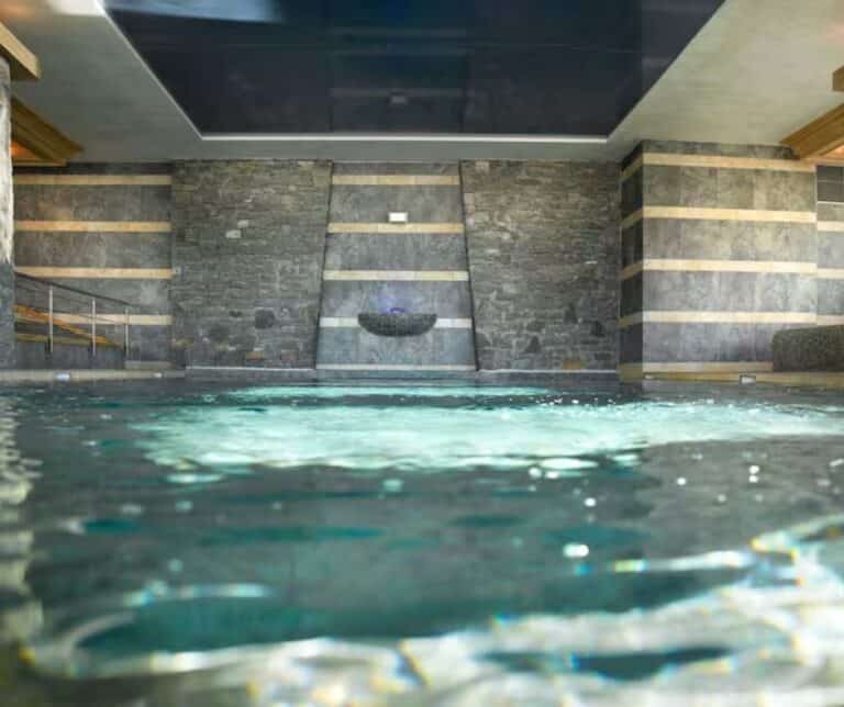 A spa pool with stone walls and horizontal wood accents, featuring a stone water feature in the center and a tranquil, softly lit atmosphere.