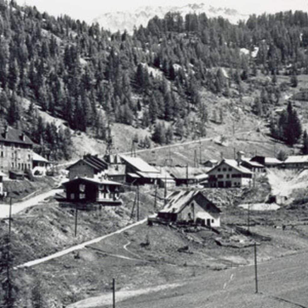 Old photograph of a small mountain village nestled in a wooded valley, showing traditional alpine houses and dirt roads before ski resort development.