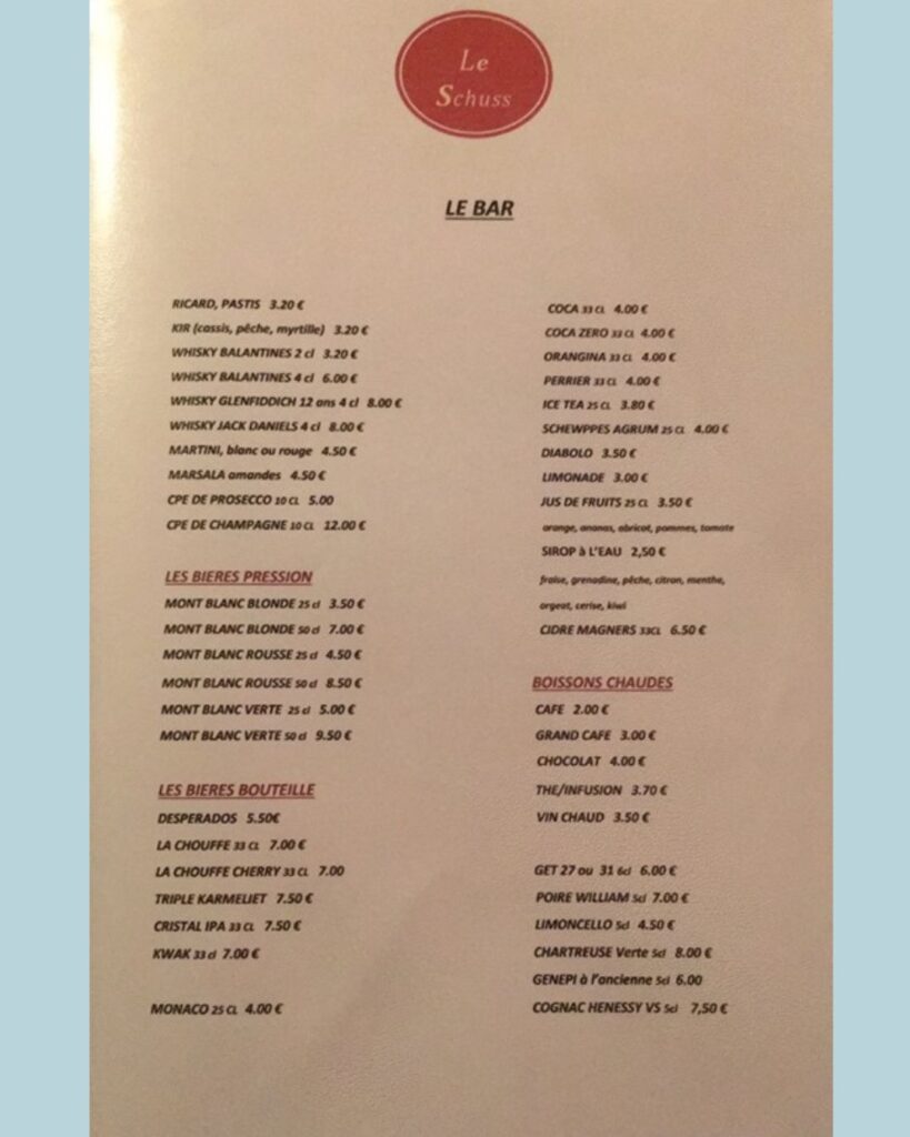 Bar menu from Le Schuss listing alcoholic beverages including beers, whiskies, wines, and cocktails, as well as non-alcoholic drinks, hot beverages, and regional liqueurs.