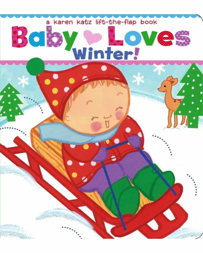 Book cover for Baby Loves Winter! by Karen Katz, showing a smiling baby bundled in a red polka dot hat and scarf, riding a red sled down a snowy hill with trees and a deer in the background.