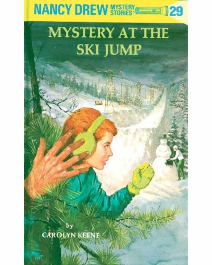 Book cover for Mystery at the Ski Jump by Carolyn Keene, showing a classic illustrated Nancy Drew peeking through pine branches in green earmuffs, as a mysterious gloved hand reaches toward her. A snow-covered ski jump and snowman are seen in the distance.
