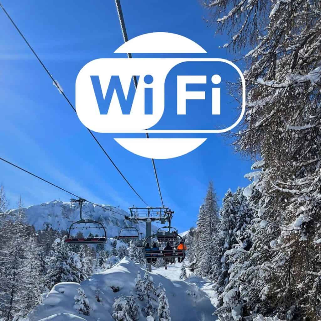A ski lift glides above a snowy alpine forest under a clear blue sky, with skiers seated and surrounded by snow-covered trees. The large white "WiFi" logo is overlaid in the center, suggesting internet access is available on the slopes.