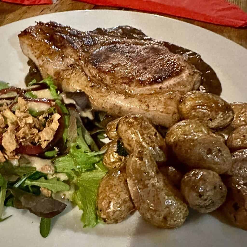 A hearty plate featuring a seared pork chop, seasoned baby potatoes, and a fresh mixed greens salad drizzled with dressing.