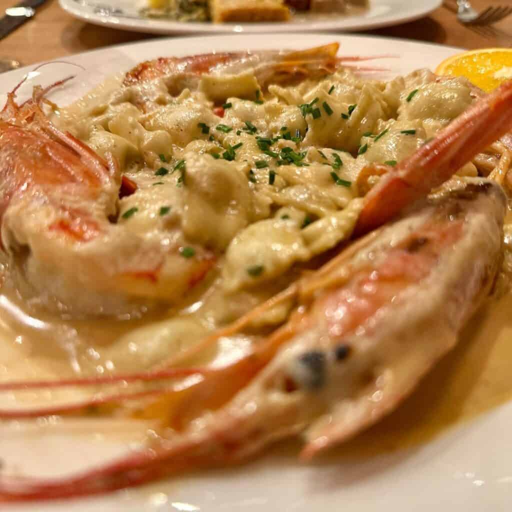 Pasta tossed in a creamy seafood sauce, garnished with chopped chives and flanked by two large whole prawns on either side of the plate.