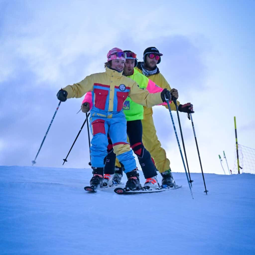 A group of skiers in matching outfits executing a synchronized formation on a well-lit slope during the Born to Be Show.​