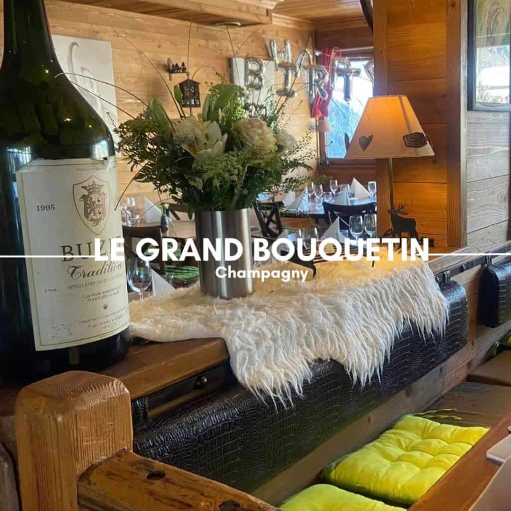 LE GRAND BOUQUETIN, Champagny – A cozy wooden restaurant with a rustic alpine ambiance, decorated with fur-covered benches, a large wine bottle, and a table adorned with fresh flowers. The warm lighting enhances the welcoming atmosphere.