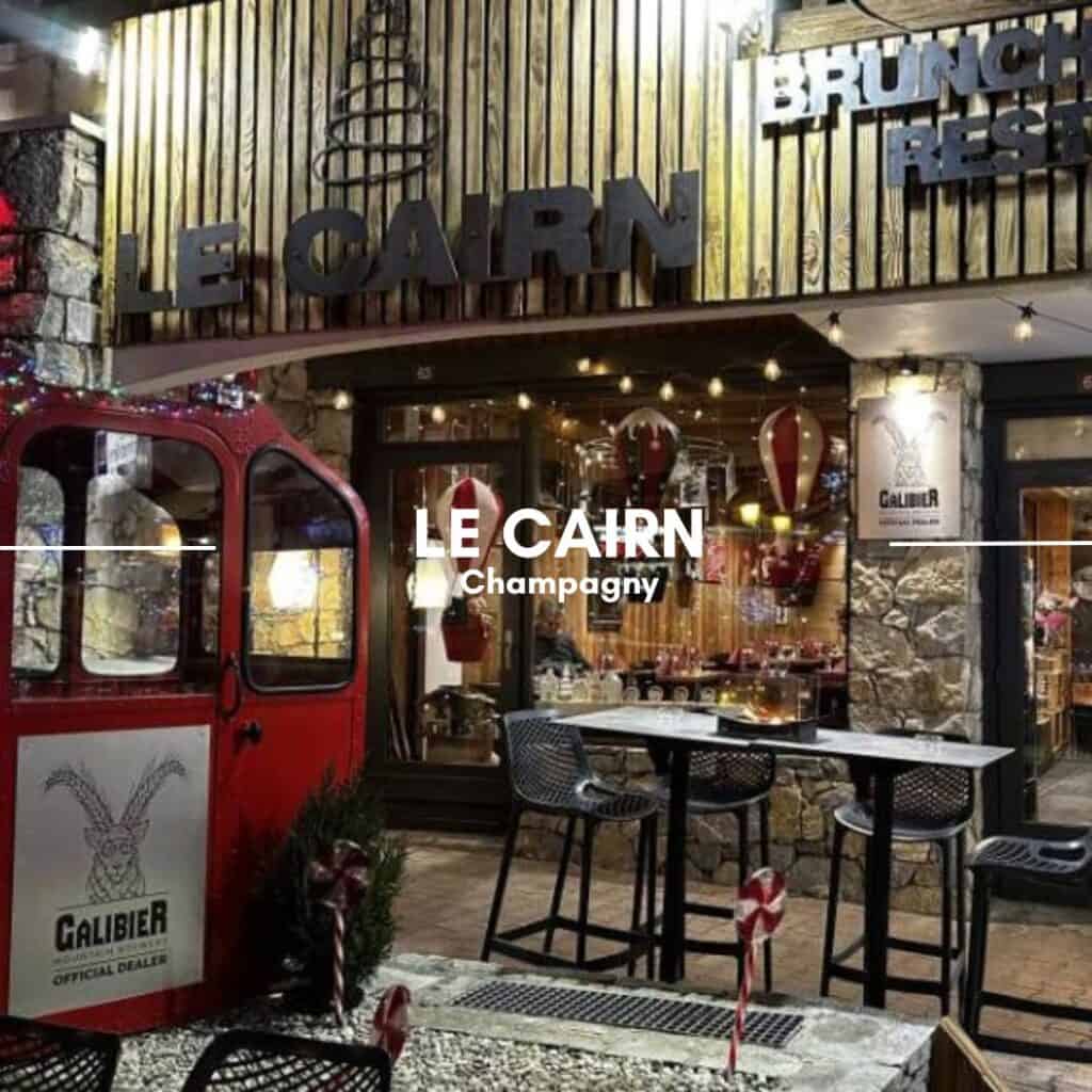 LE CAIRN, Champagny – A stylish, modern restaurant with an illuminated wooden facade and outdoor seating. A vintage red cable car sits outside, adding to the mountain-inspired decor.