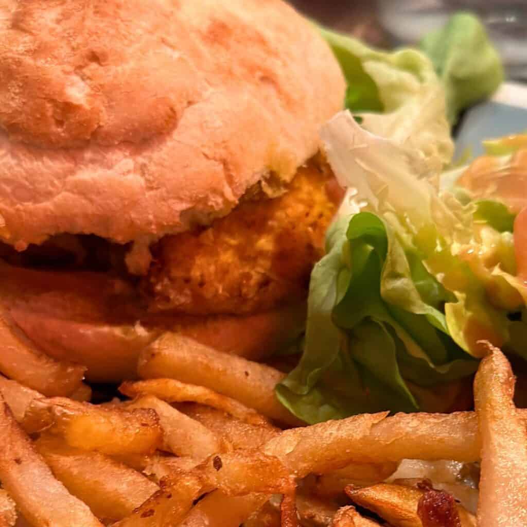 Close-up of a crispy halal chicken burger served with golden French fries and a side of fresh lettuce and tomato salad in La Plagne. The sandwich features a toasted bun and juicy, well-seasoned patty, perfect for showcasing the best halal food in la plagne.