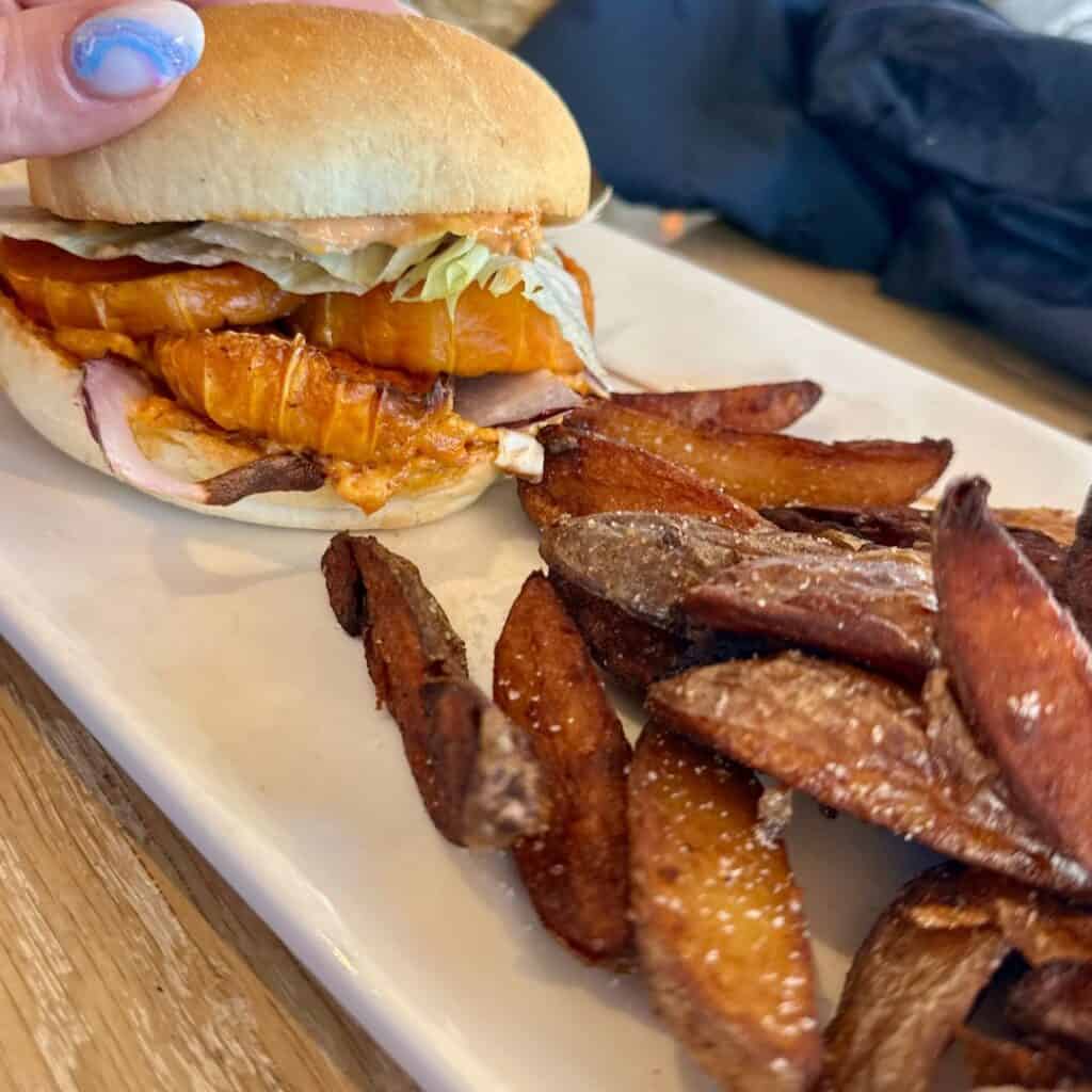 A plate of golden, crispy potato wedges paired with a sandwich filled with melted cheese, ham, and lettuce, held by a person with blue-painted nails. At Le Chairlift restaurant, La Plagne.