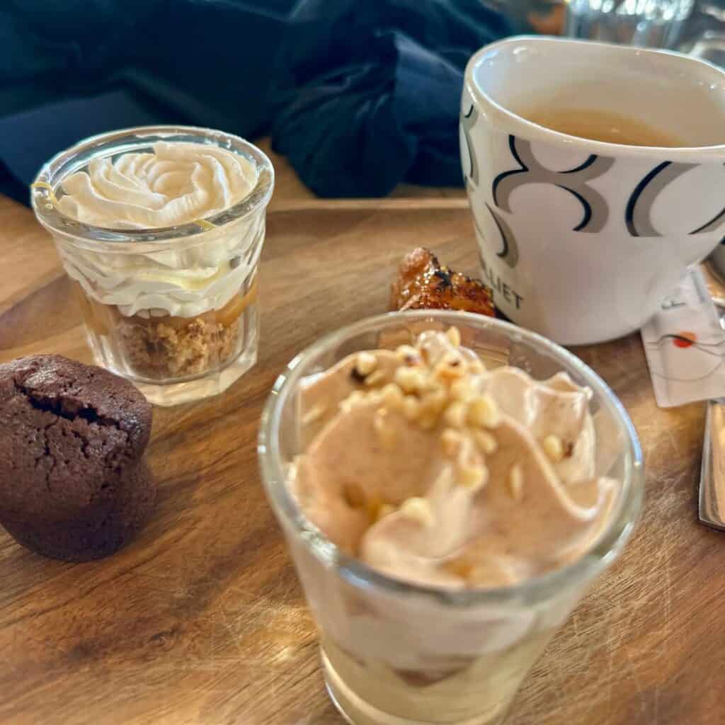 A wooden dessert tray featuring small glass cups filled with whipped cream, mousse, and nuts, alongside a molten chocolate cake and a cup of espresso. At Le Chairlift restaurant, La Plagne.