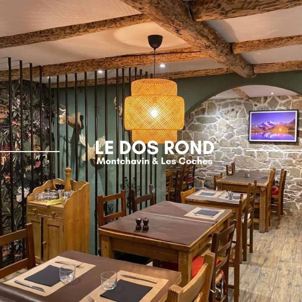 A warmly lit restaurant with wooden tables, stone walls, and decorative wooden beams. A woven pendant light hangs in the center, and the walls feature artwork and nature-inspired designs. The text overlay reads "Le Dos Rond, Montchavin & Les Coches."