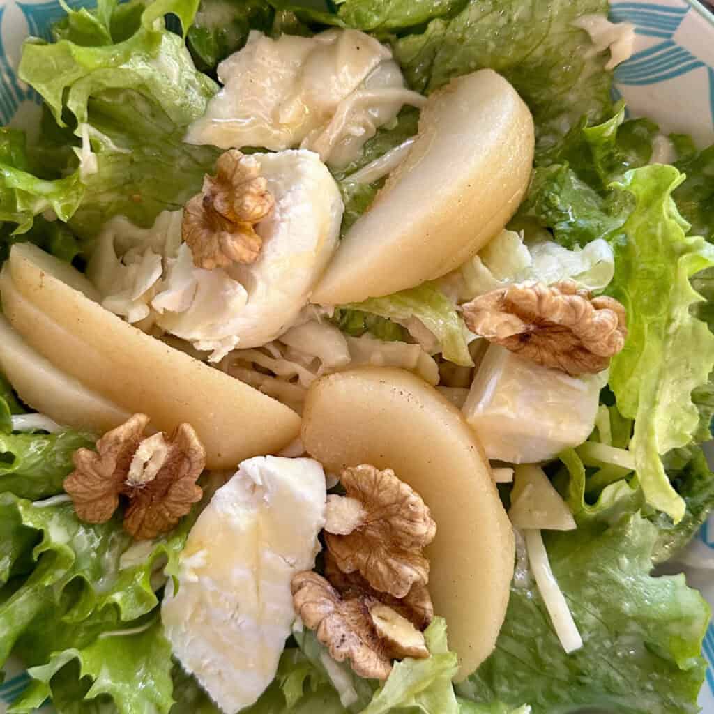 A close-up of a fresh salad served at Chalet du Plan Bois, featuring crisp green lettuce, creamy slices of brie cheese, poached pear wedges, and crunchy walnuts.