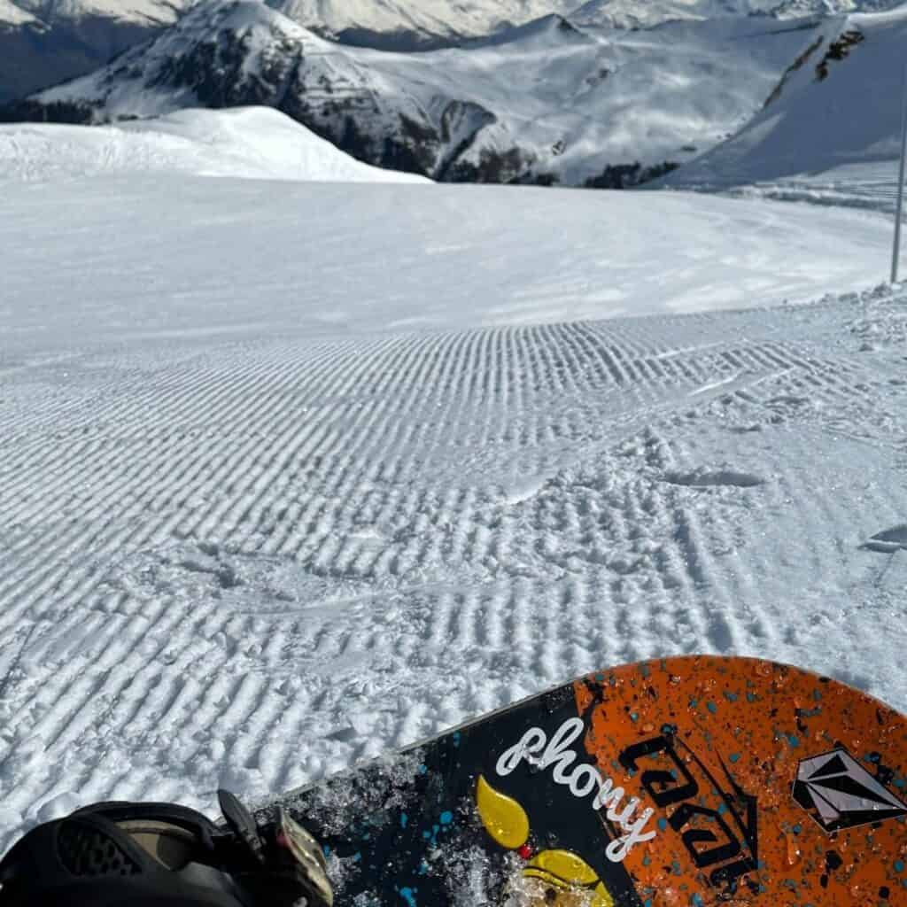 Snowboard resting on crisp corduroy snow with a mountain backdrop in La Plagne, where the terrain suits adrenaline-seekers whether they prefer skiing or snowboarding.