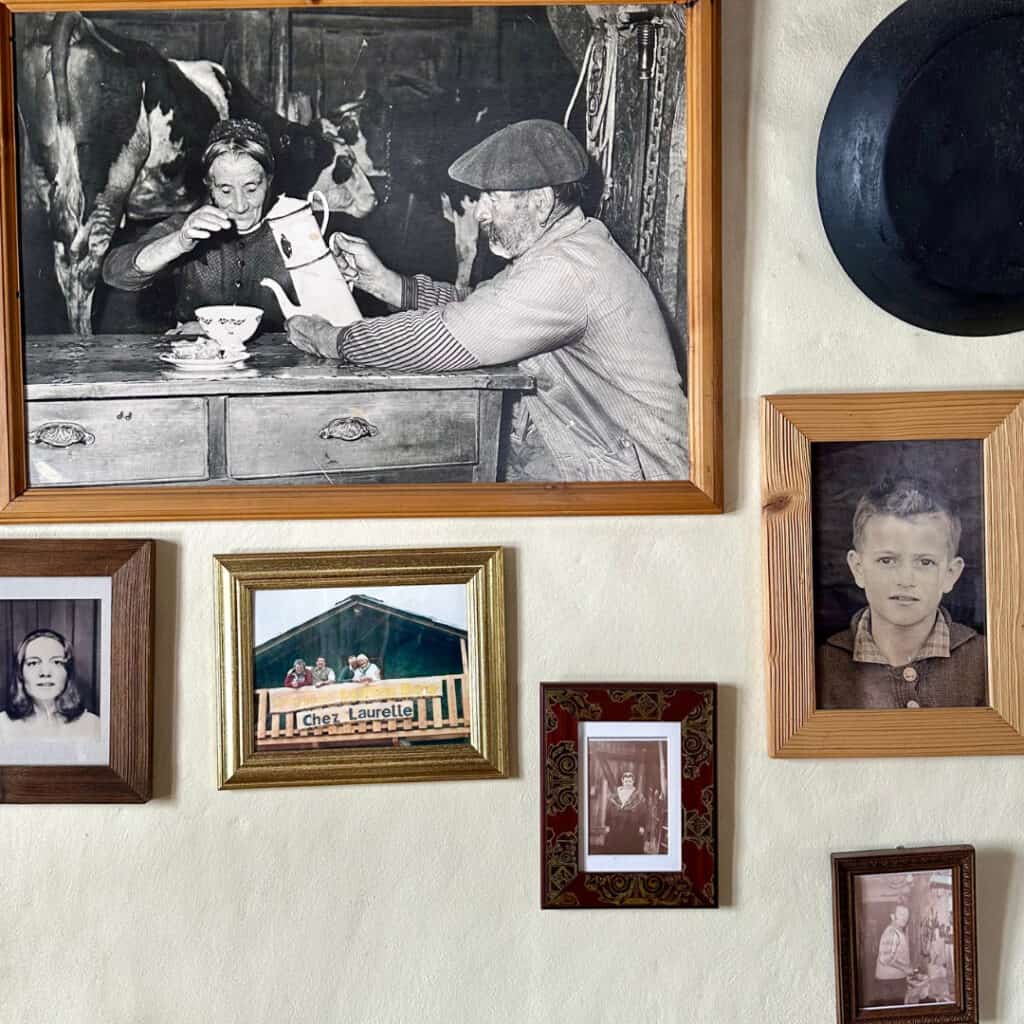 A wall inside Chalet du Plan Bois decorated with vintage family photographs and a nostalgic black-and-white portrait of a couple sharing coffee in a barn.