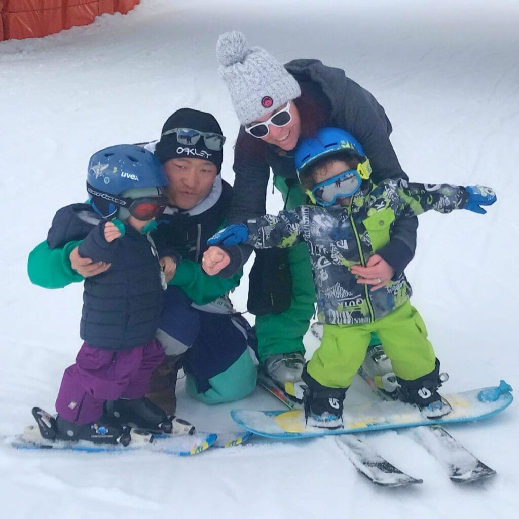 A family with two kids—one on skis, one on a snowboard—poses happily on a gentle slope, showing how La Plagne caters to families no matter if they're into skiing or snowboarding.