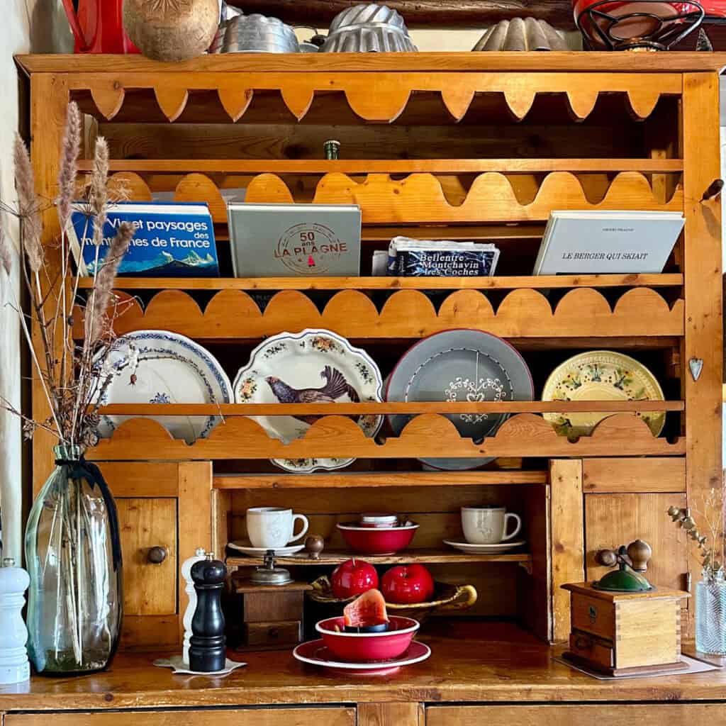 A wooden hutch inside Chalet du Plan Bois filled with decorative plates, ceramic cups, cookbooks, and alpine-style knickknacks, adding to the rustic mountain charm.
