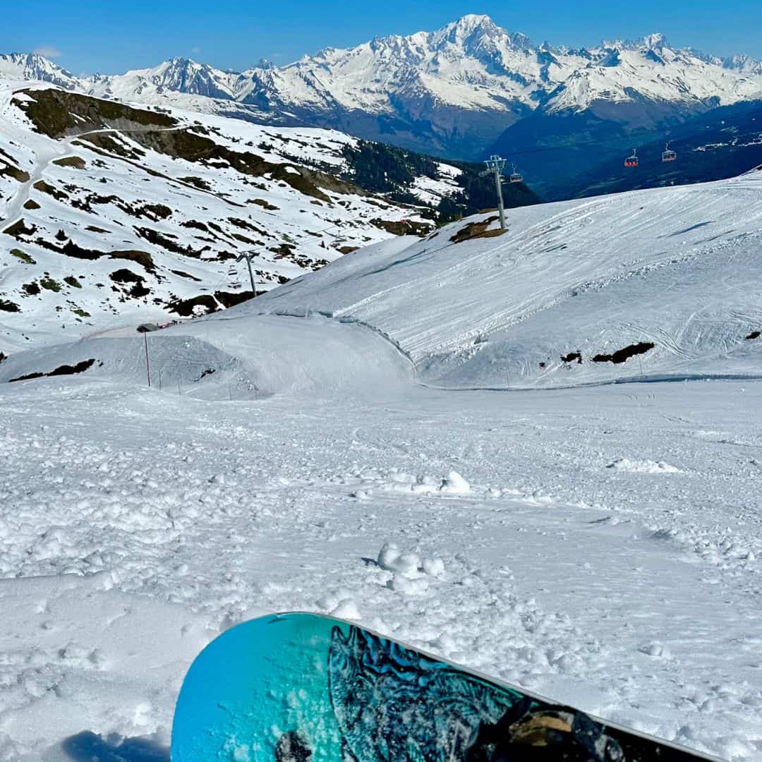 A snowboarder sits at the top of a broad slope in La Plagne with a clear view of the surrounding mountains, highlighting the epic terrain available for both skiing or snowboarding in La Plagne.