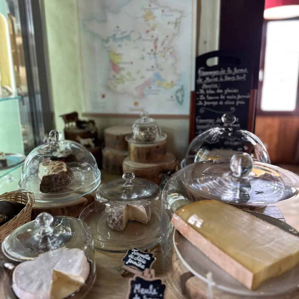 An artisanal cheese selection at Chalet du Plan Bois displayed under glass domes, featuring aged cheeses on wooden risers with a map of French wine regions in the background.