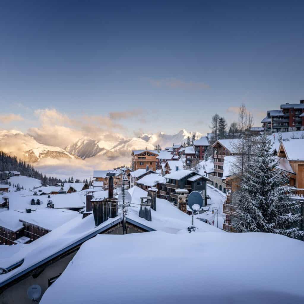 Snow-covered rooftops of La Plagne at dusk with sunlit mountains in the background, capturing the stunning setting of the area’s best alpine accommodation.