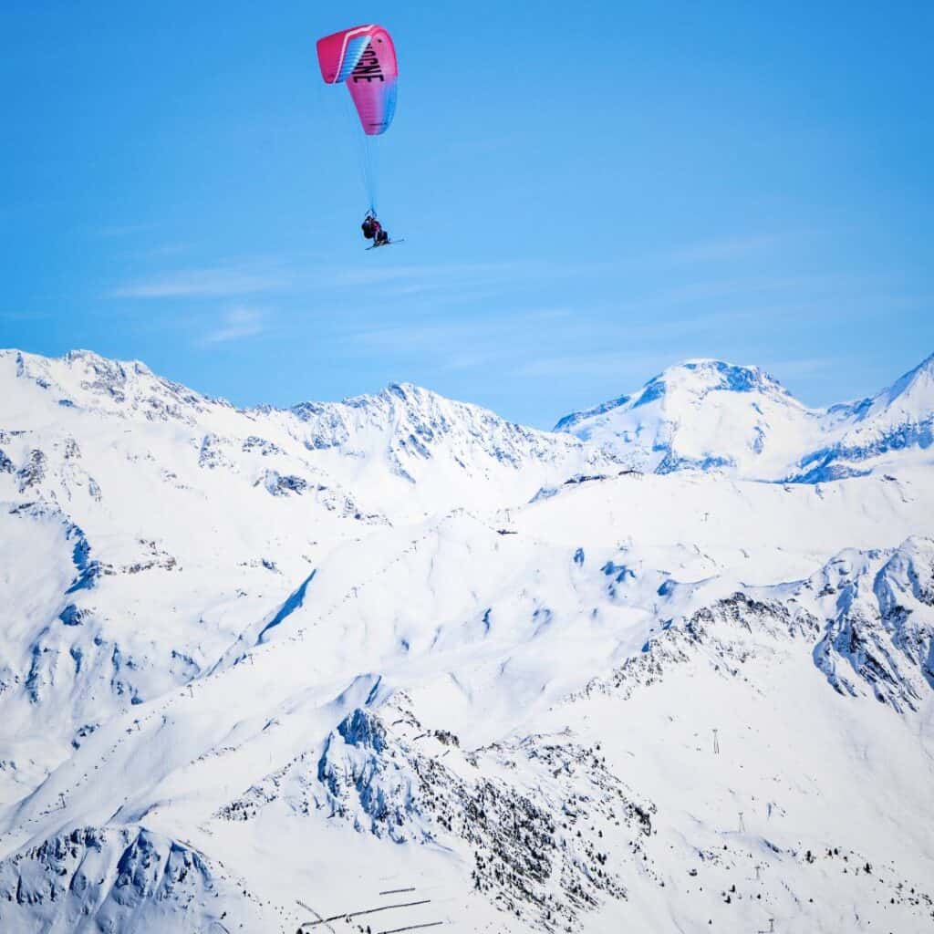 A paraglider soars high above the snow-covered Alps near Belle Plagne, offering a thrilling view close to the best accommodation Belle Plagne has for adventure seekers.