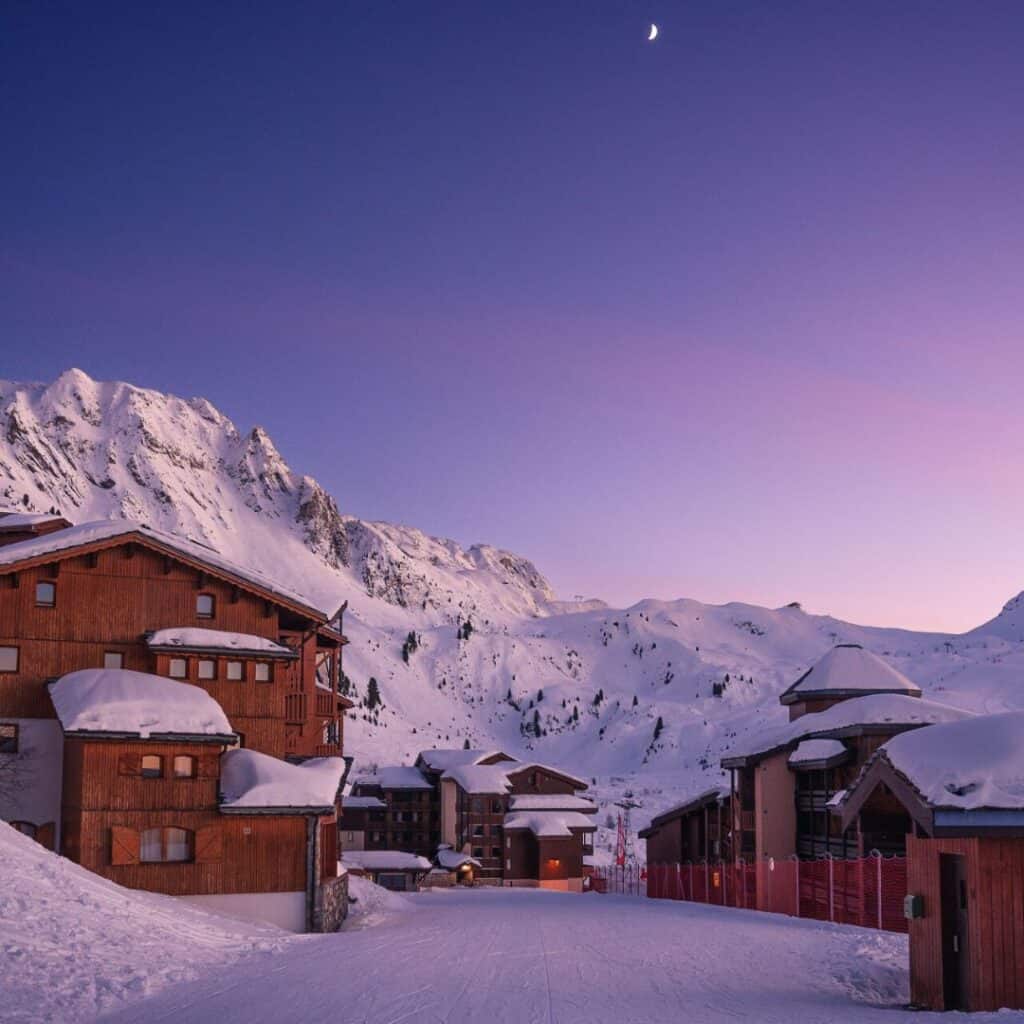 Purple twilight settles over Belle Plagne’s snowy chalets and ski runs beneath a crescent moon, capturing the peaceful charm of the best accommodation Belle Plagne.