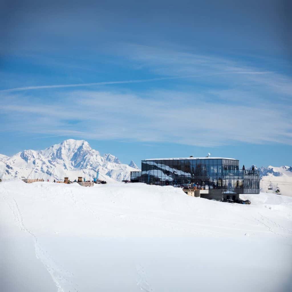 Le 360 restaurant in Montalbert, La Plagne, with its sleek glass exterior reflecting the snow and sky, offers stunning panoramic views of Mont Blanc. It's an ideal picnic spot for scenic breaks or enjoying your lunch on the surrounding sunny terrace.