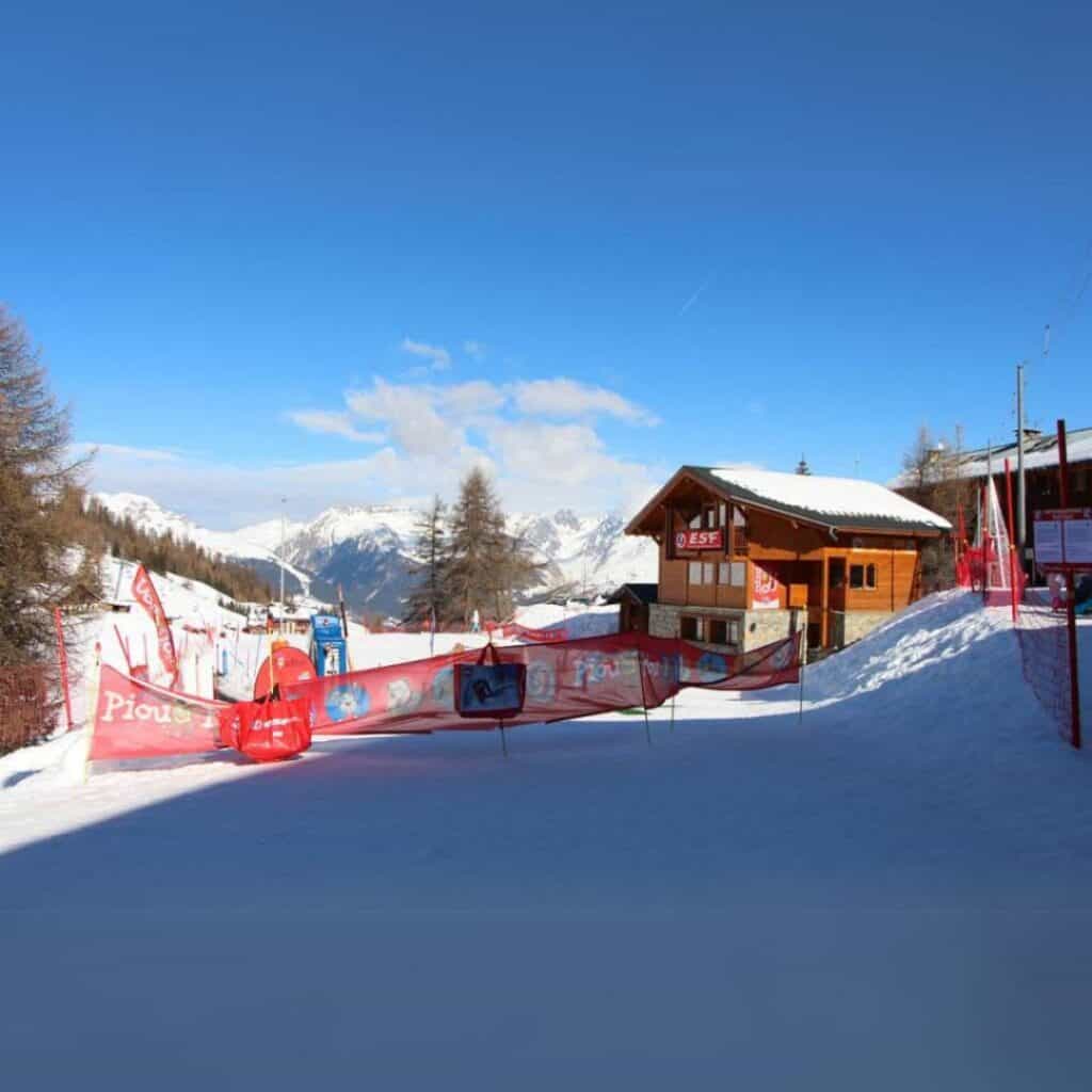 The ESF ski school area in La Plagne with red signage and fencing, ideal for families staying in nearby accommodation with easy ski school access.