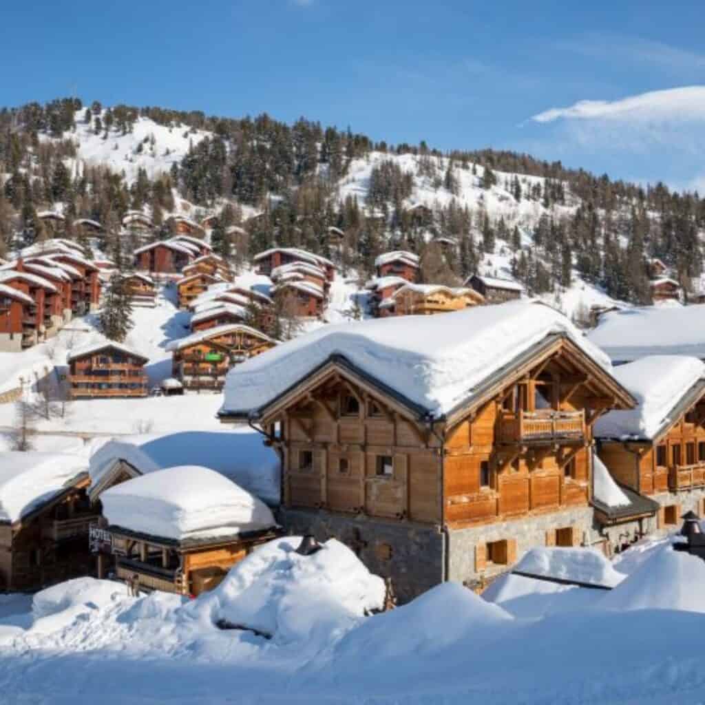 Charming wooden chalets tucked into the hillside under deep snow, showcasing some of the best accommodation in La Plagne for a scenic mountain escape.