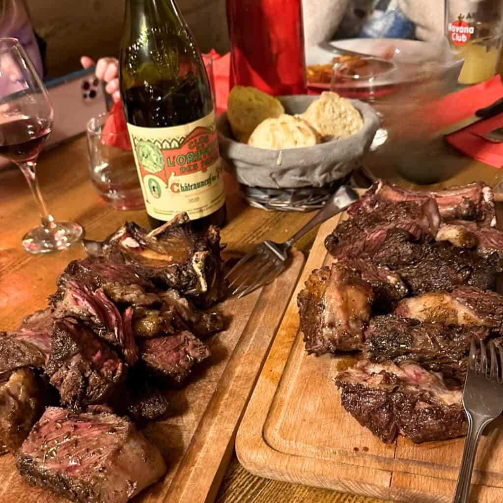 A rustic alpine dinner setup with grilled meat, red wine, and fresh bread, reflecting the hearty dining experiences available near top La Plagne accommodation.