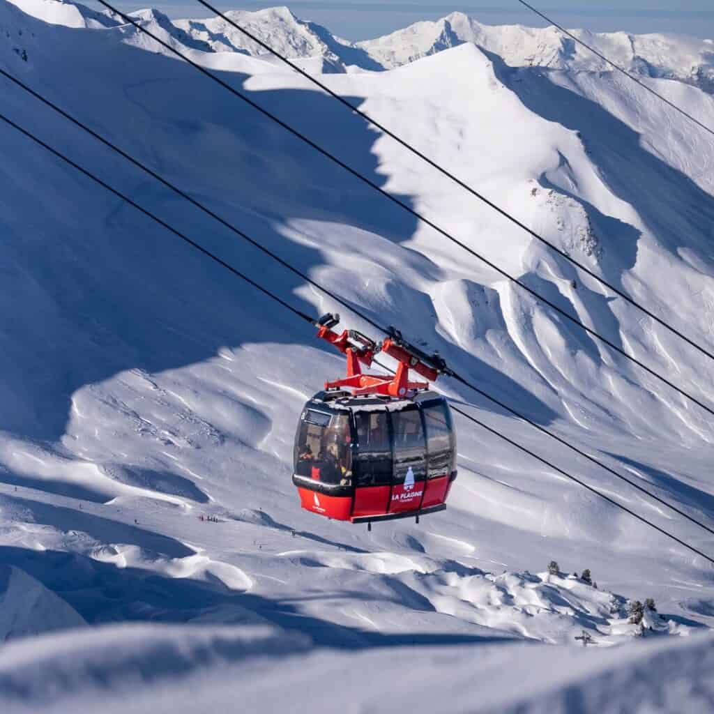 La Plagne’s iconic red gondola soars above snow-covered slopes, easily accessible from the best accommodation Plagne Centre for ski and sightseeing adventures.