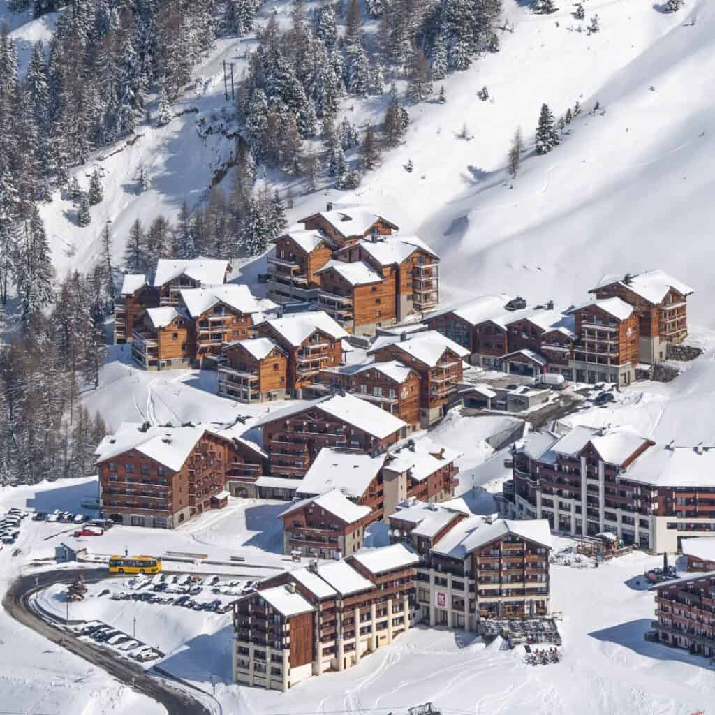 Aerial view of snow-covered chalets and apartments nestled in the mountains, showing the layout of self catering La Plagne accommodations near ski slopes.