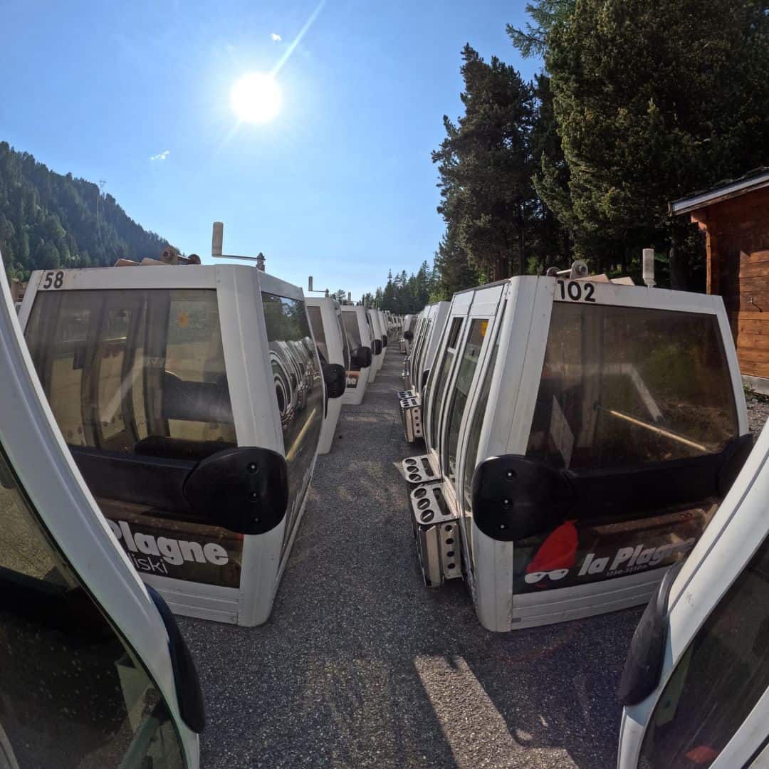 Rows of retired bubble lift gondolas from La Plagne ski resort are lined up outdoors under a bright alpine sun, awaiting new owners as part of a public sale. Each cabin is numbered and branded with the La Plagne logo, offering ski fans a unique piece of mountain memorabilia.