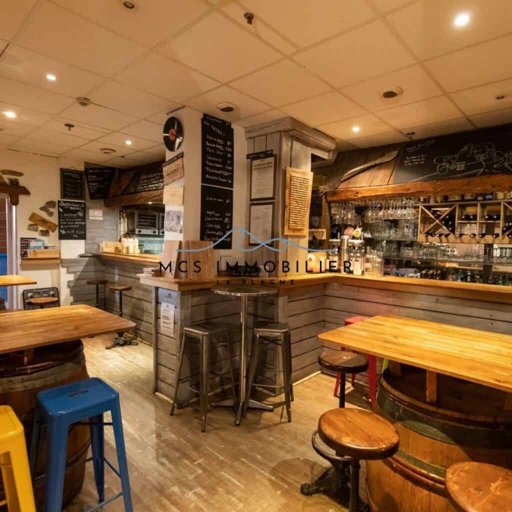 Warm and inviting wooden bar interior featuring rustic stools, chalkboard menus, and shelves stocked with glasses and bottles.