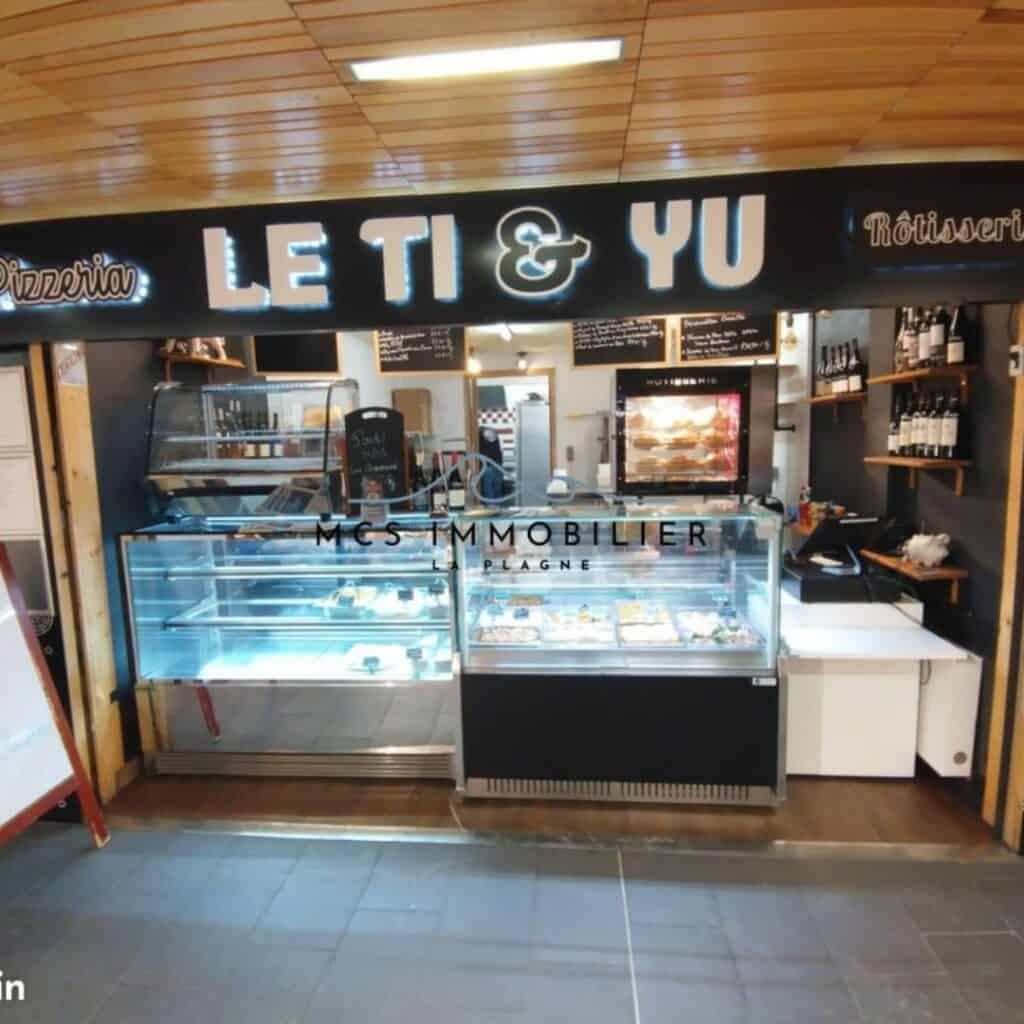 Modern food counter inside a commercial space labeled “Le Ti & Yu” offering pizzeria and rotisserie options with glass display cases showcasing prepared dishes.