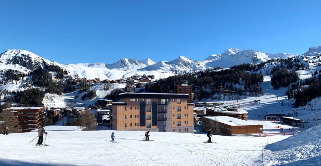 Scenic view of skiers on a snowy slope in La Plagne with Hotel Graciosa in the background, illustrating the direct slope access and stunning setting of this VIP SKI destination.