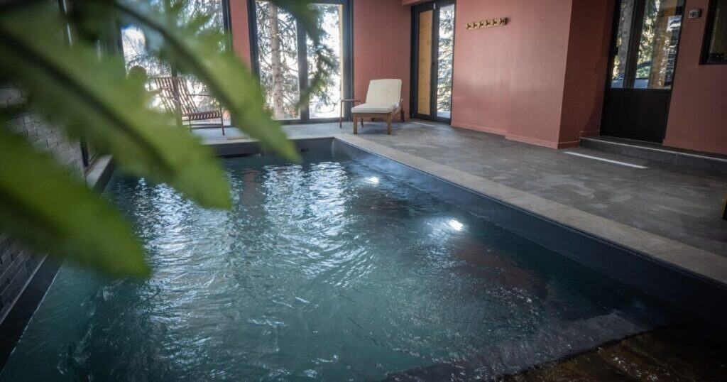 Heated indoor swimming pool at Chalet du Bois Melay in La Plagne, with seating areas and large windows looking onto snow-covered forest from this luxury chalet.