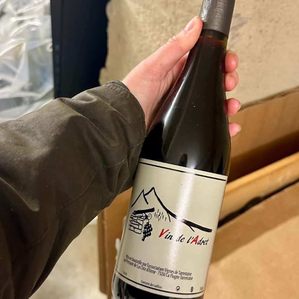 Close-up of a hand holding a bottle of Vin de l’Adret featuring a mountain illustration, produced in La Plagne Tarentaise.