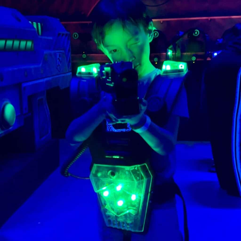 Child playing laser tag in a dark neon lit arena holding a glowing blaster. Immersive game experience at K Park Albertville perfect for a trampoline park Albertville visit.