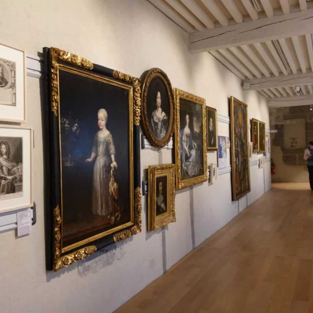Gallery wall filled with framed historic portraits in ornate gold frames inside a museum. Cultural experience to include on a day trip from La Plagne.