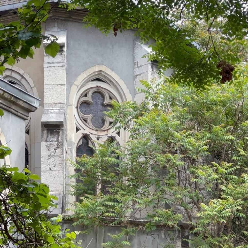Stone building partially hidden by greenery with gothic style window details. Scenic architecture found while wandering Chambéry on a family day trip French Alps.