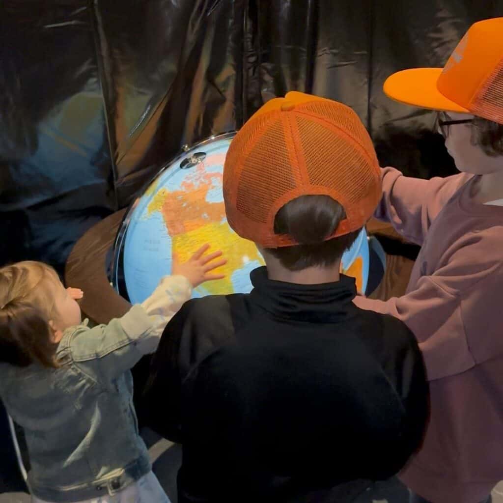 Children gathered around a globe exhibit inside a museum exploring geography together. Hands on learning during a day trip from La Plagne.