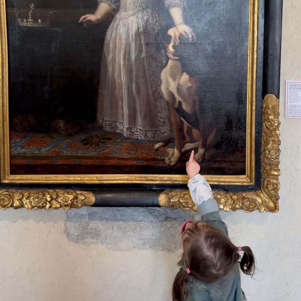 Child pointing at a painting of a dog inside a museum framed in gold. Engaging art moment during a day trip from La Plagne.