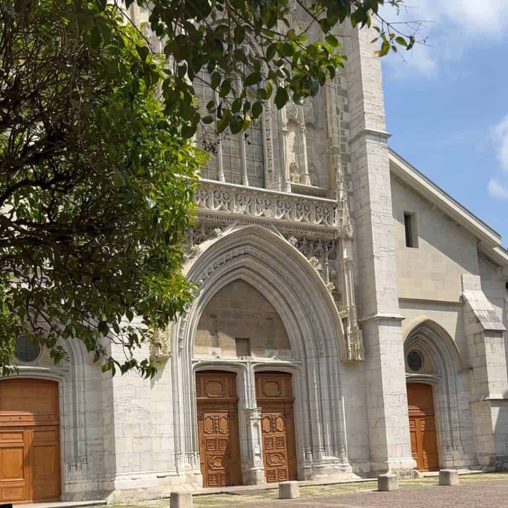 Large cathedral facade with detailed stonework and wooden doors under a blue sky in Chambéry. Impressive stop on a day trip from La Plagne.